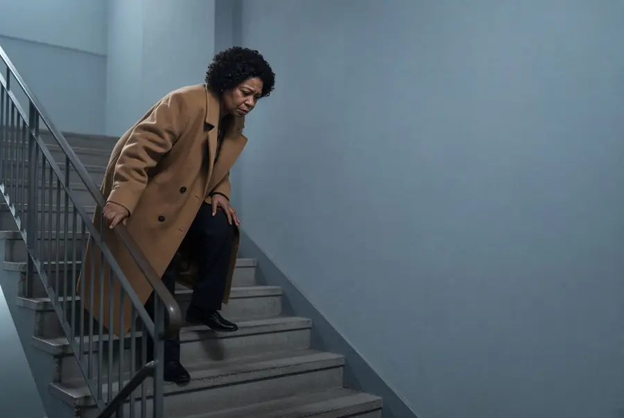 Woman pausing on a staircase with a hand on the railing and the other on her knee